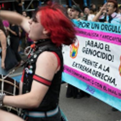 Participants holding a banner at an LGBTIQ+ and student pride march, with various signs and a crowd in the background.
