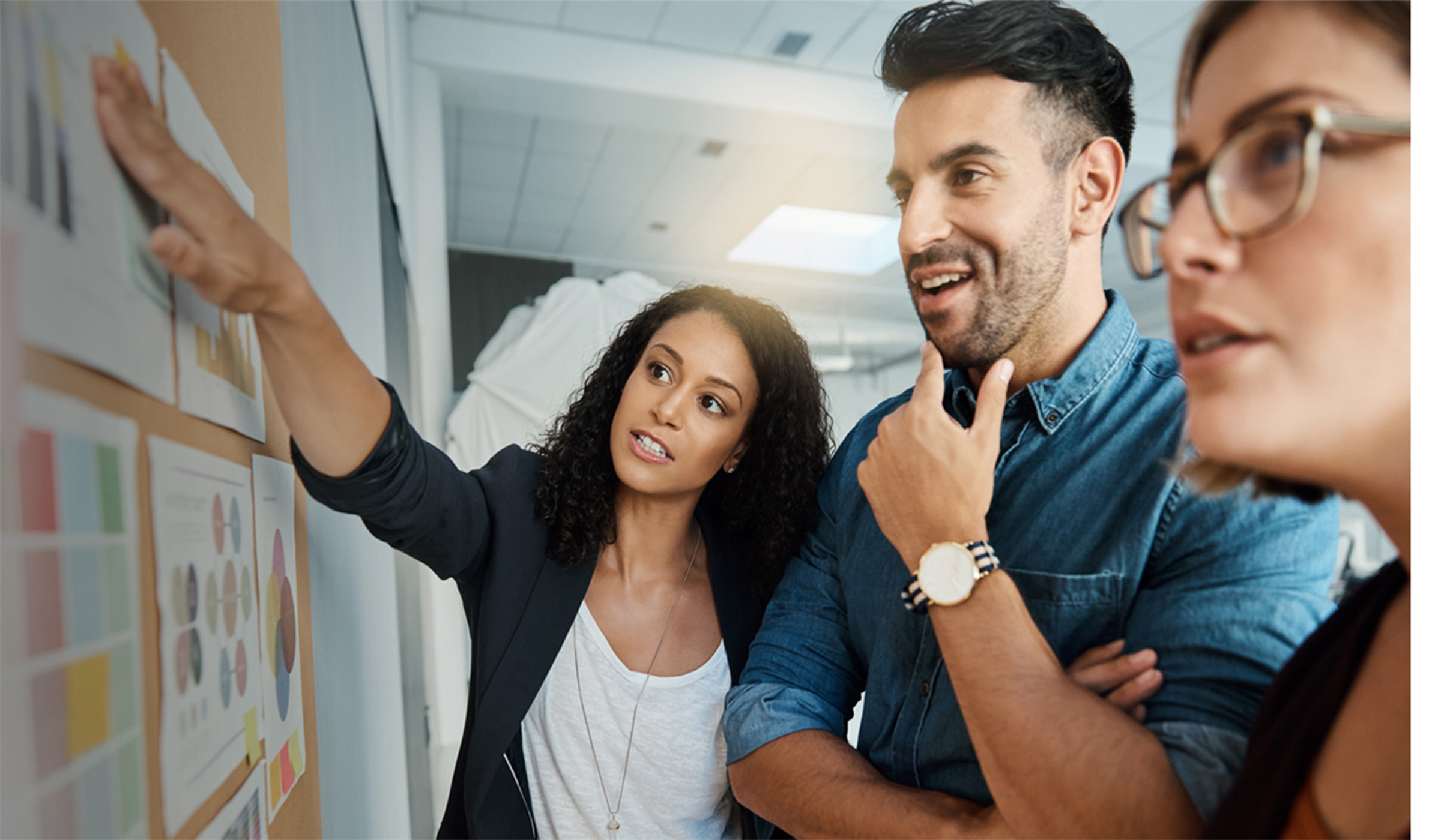 Three coworkers looking at pinned project management documents on a billboard