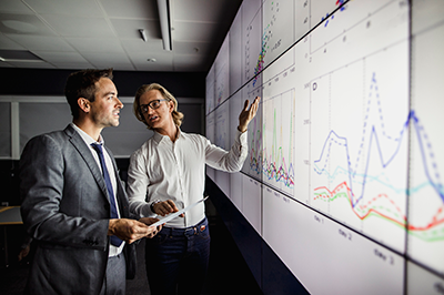 two men in front of screen with graphs