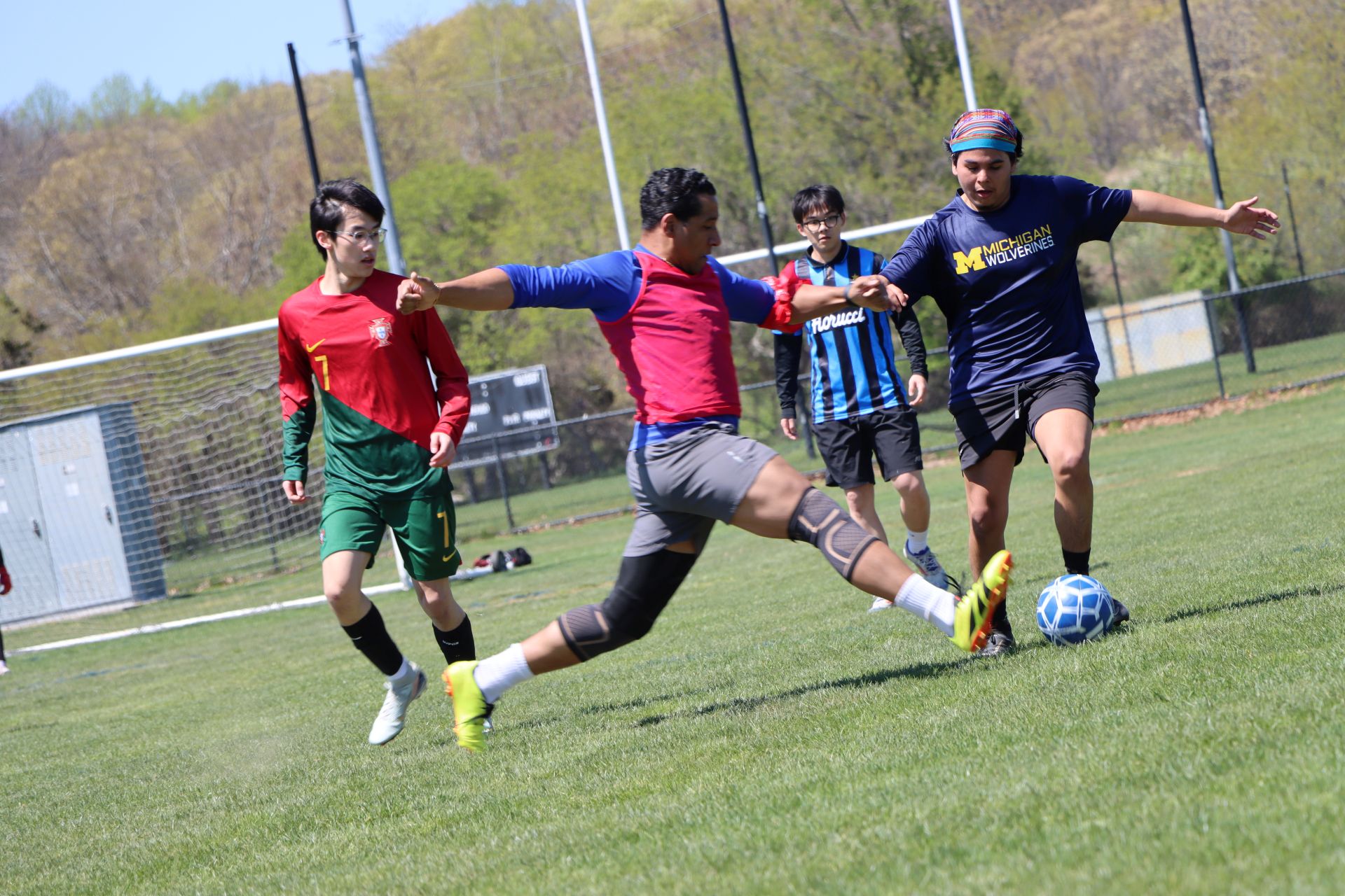 Students and alumni playing soccer on a sunny day.