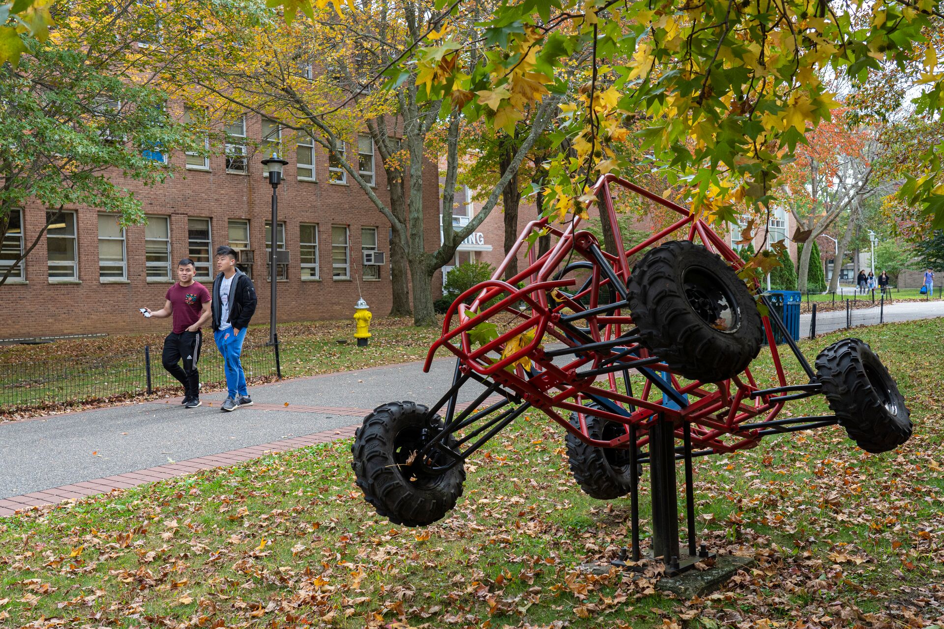 Students walking outside near a sculpture of an off-terrain vehicle.