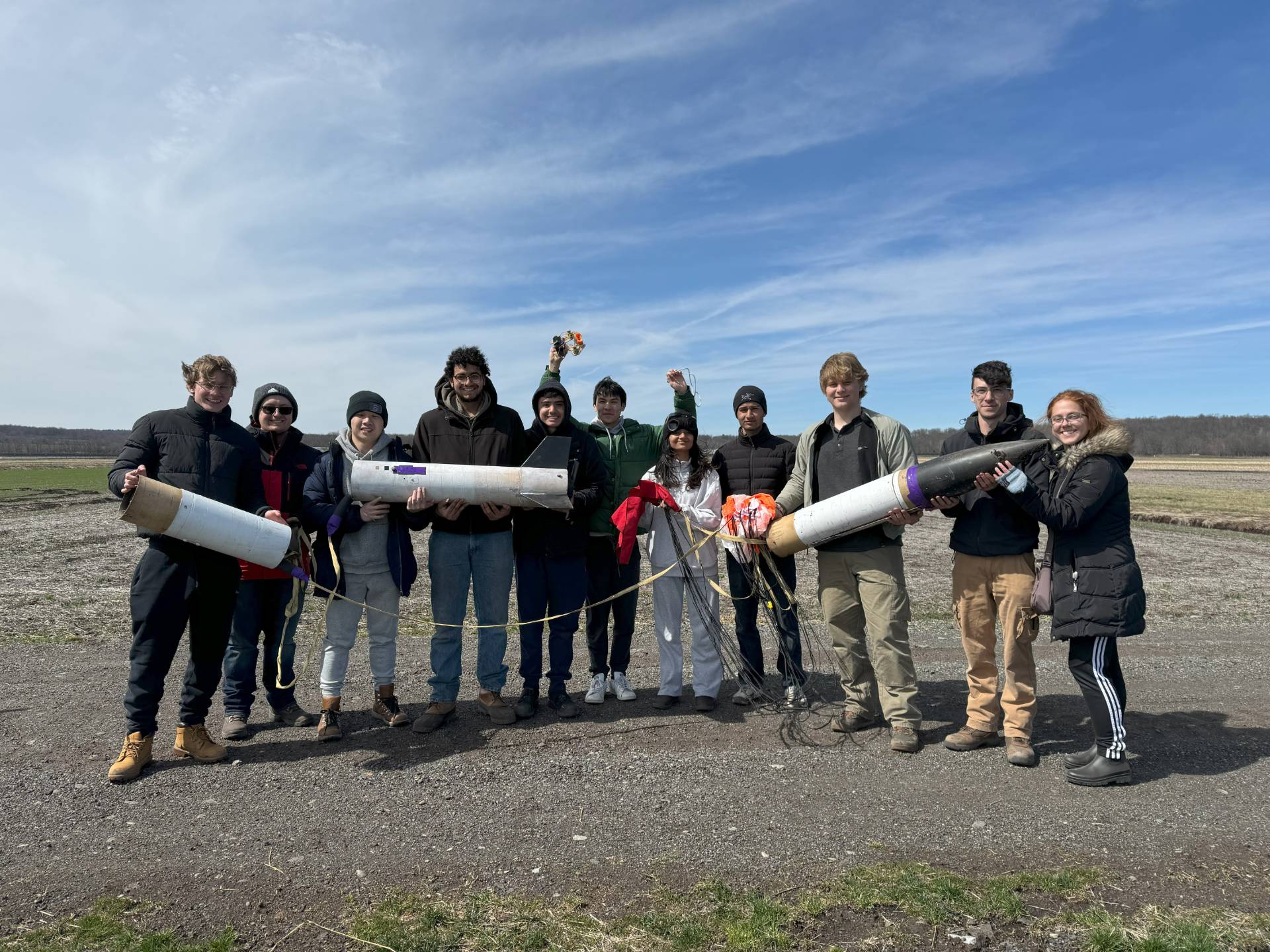Eleven people holding different parts of a rocket outside.