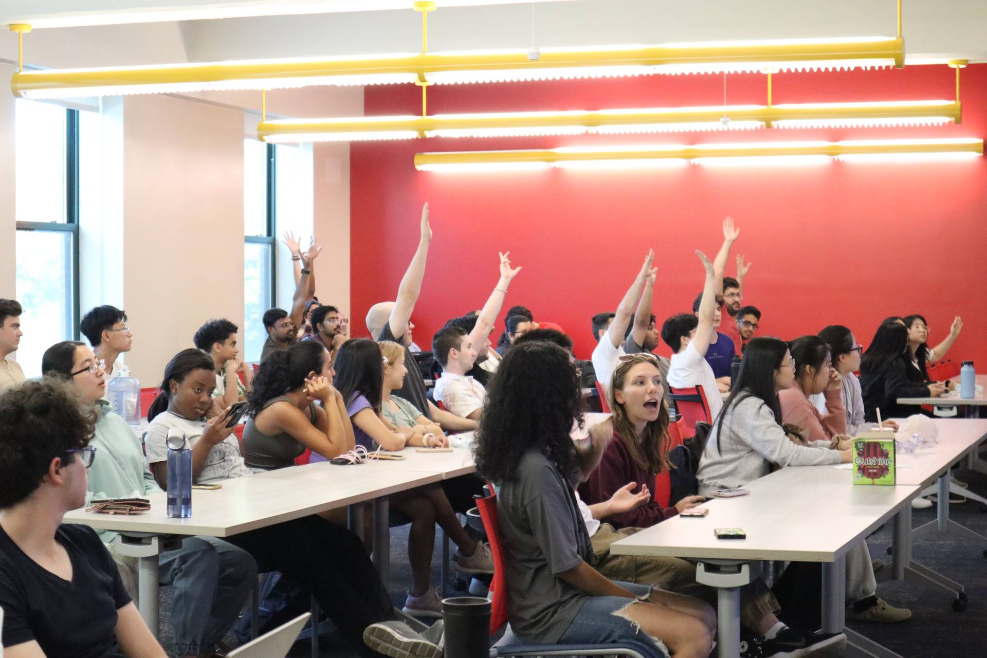 A group of people sitting at tables with their hands raised.