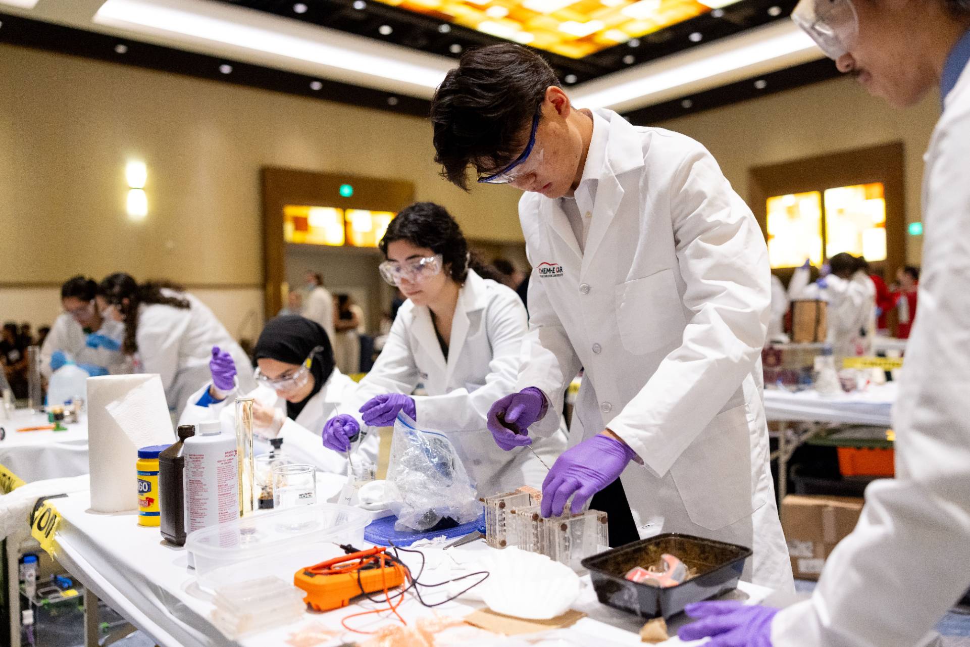 Students wearing lab coats and using chemicals at a table.