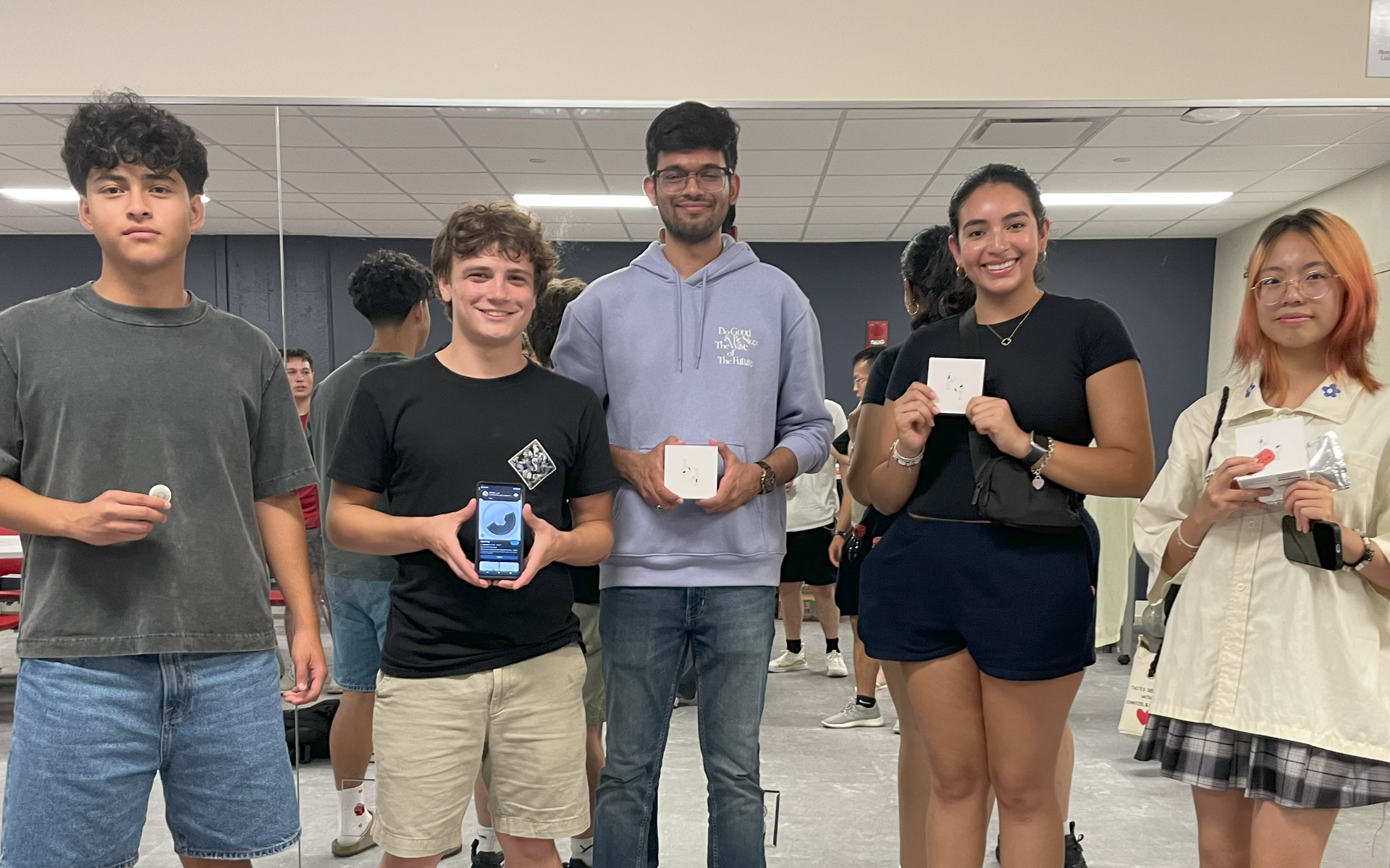 Five students holding prizes in front of a mirror backdrop.