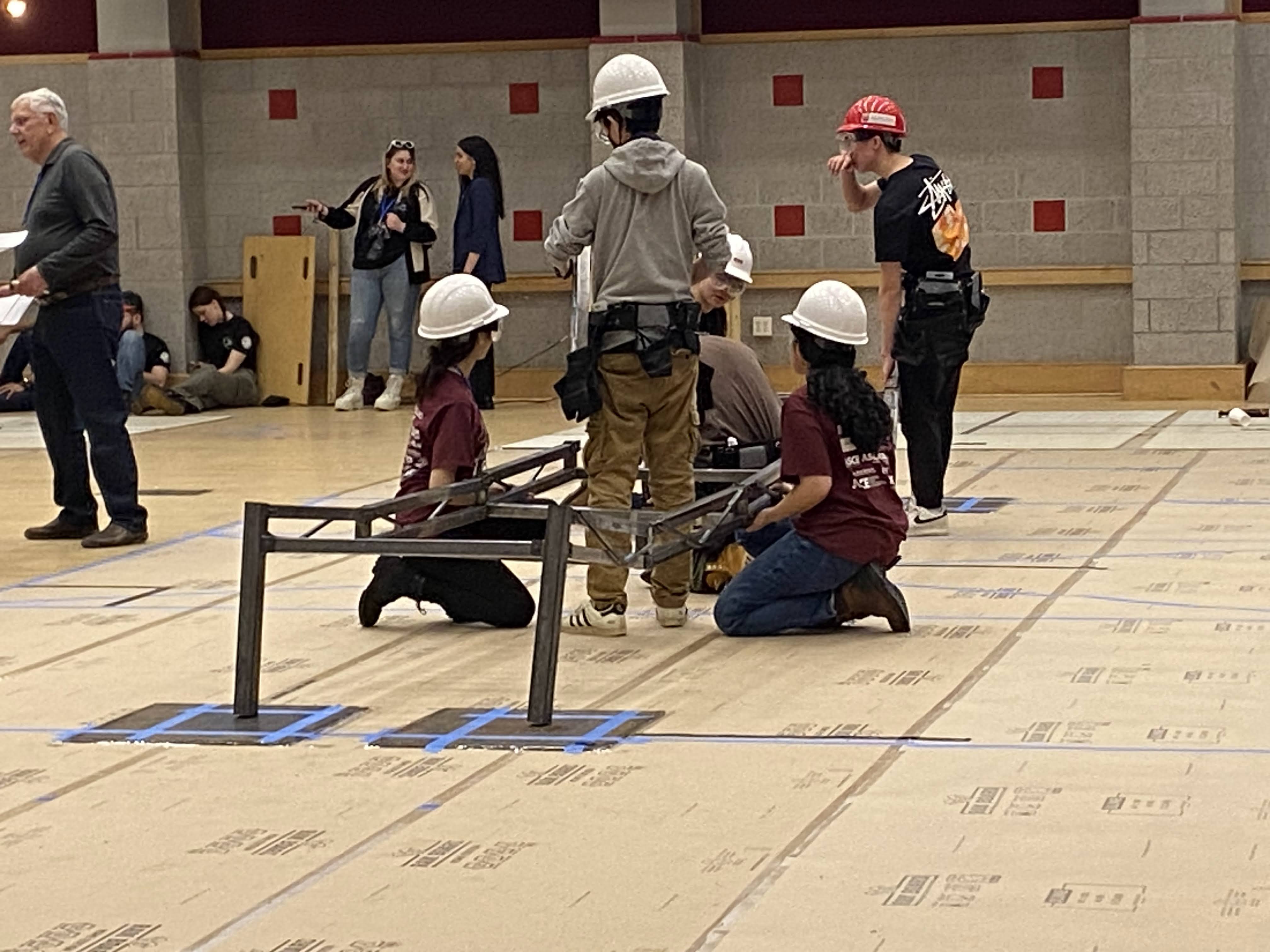 Students wearing hard hats working in a large room.