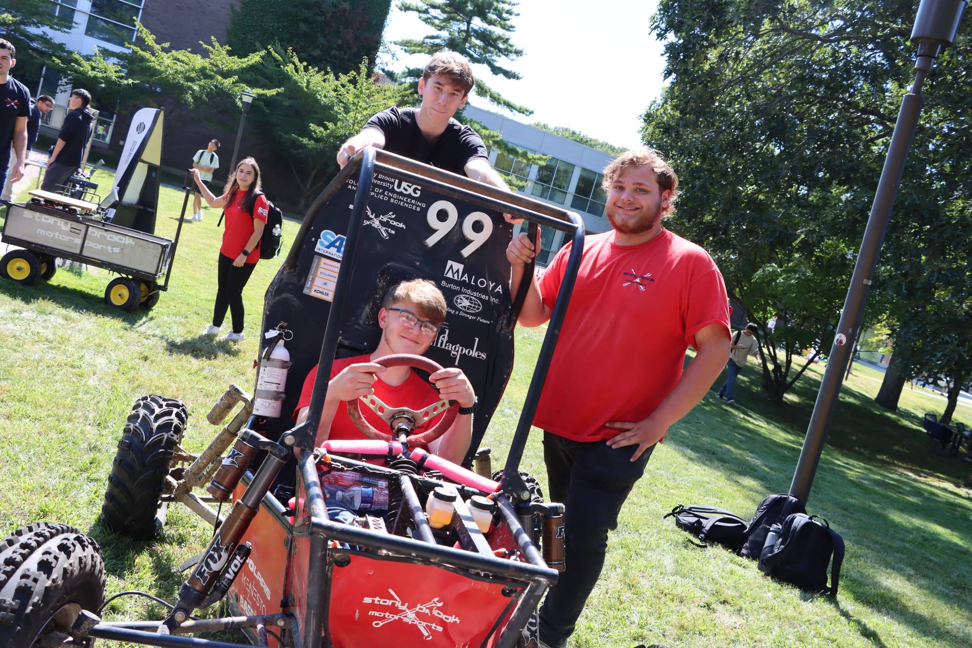 Three students posing against the off-terrain vehicle outside.