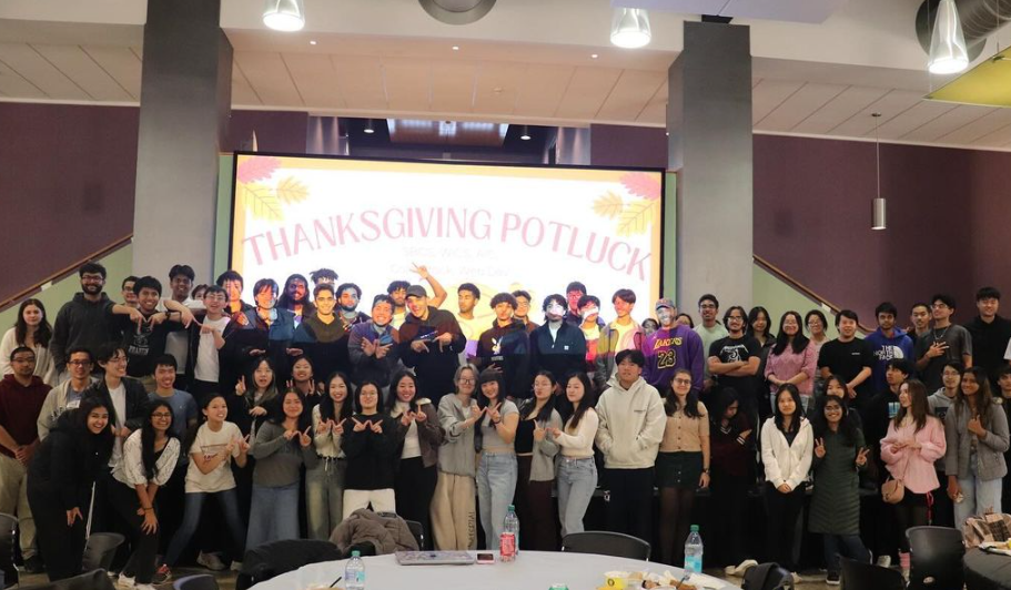 A group of students taking a photo with a banner that says Thanksgiving Potluck in the background.