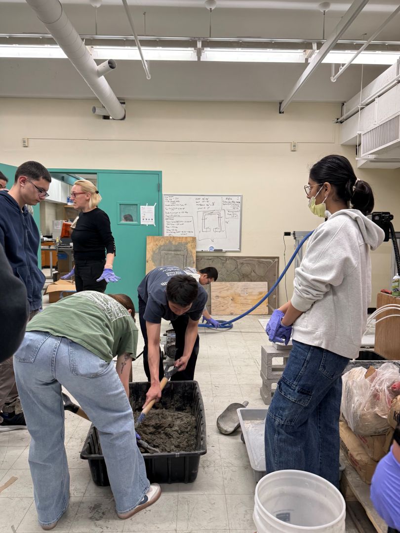 Students working in a lab, using tools to mix concrete in a large bin. 