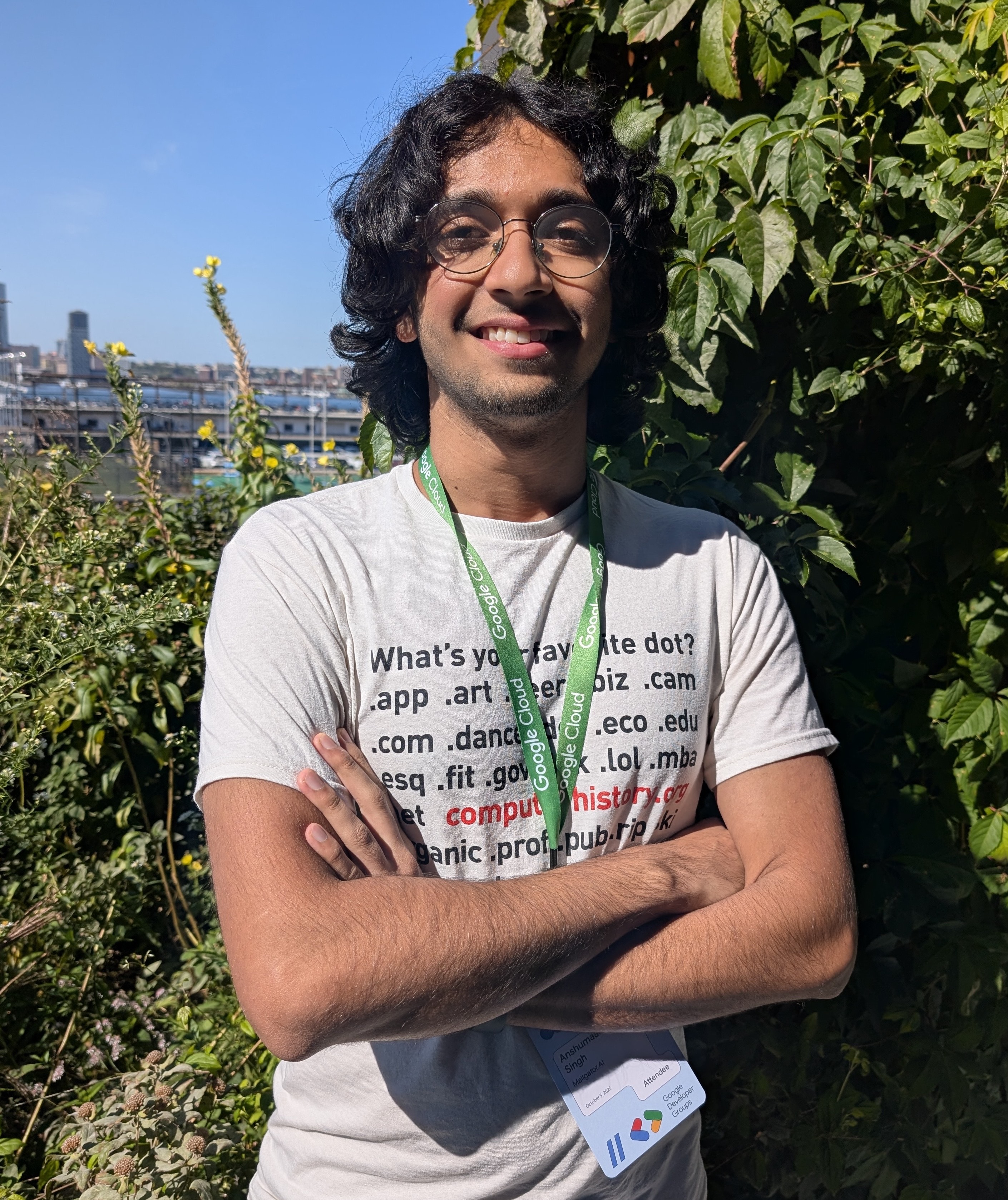 Manas posing in front greenery, arms crossed and smiling.