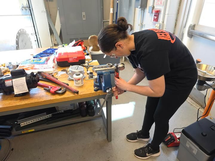 Hailee working at a bench with tools and a camp.