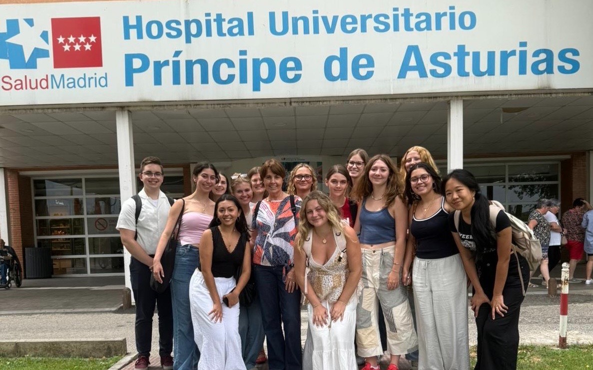 Group of students posing outside with a sign for a university hospital in Spain.