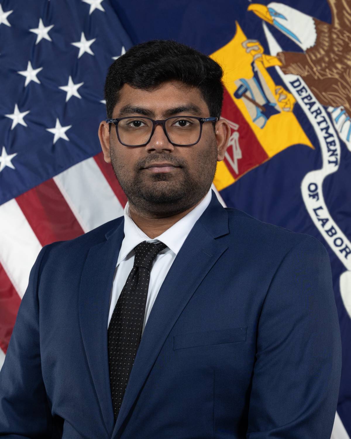 Dev portrait with the American flag and Department of Labor flag in the background.
