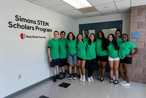 Simons STEM Scholars Ten smiling students in green t-shirts and shorts next to the Simons Center sign