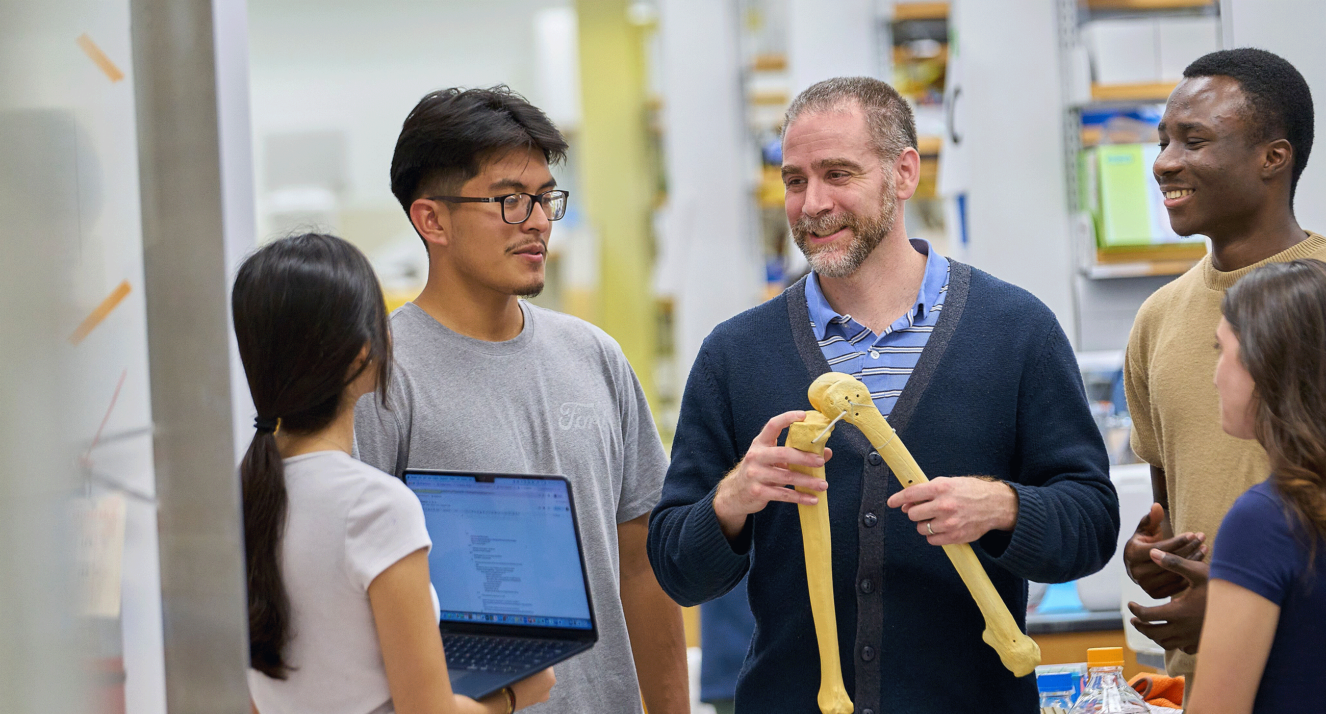 Professor holding fake bones surrounded by students