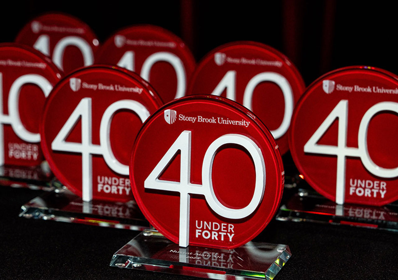 Red circular awards with "40 Under Forty" from Stony Brook University arranged on a black surface.