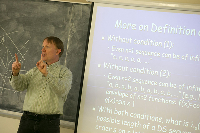 Joseph Mitchell, Chair of AMS, teaching in front of a blackboard with a slide to his right with mathematics
