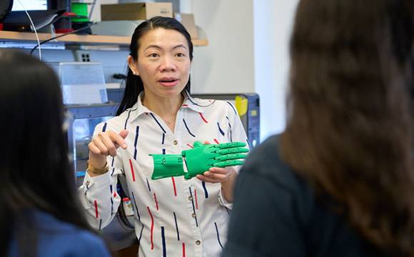 Mei-Lin Ete Chan, a professor of biomedical engineering, is talking to two students and she is holding a robotic green hand.