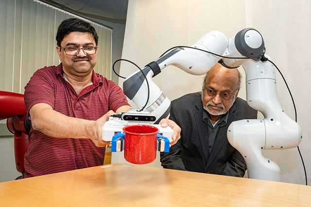 Two professors with a robotic arm are seated at a table