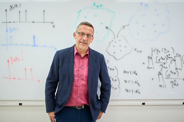 Professor Peter Djuric standing in front of the classroom, smiling, with hands in his pockets