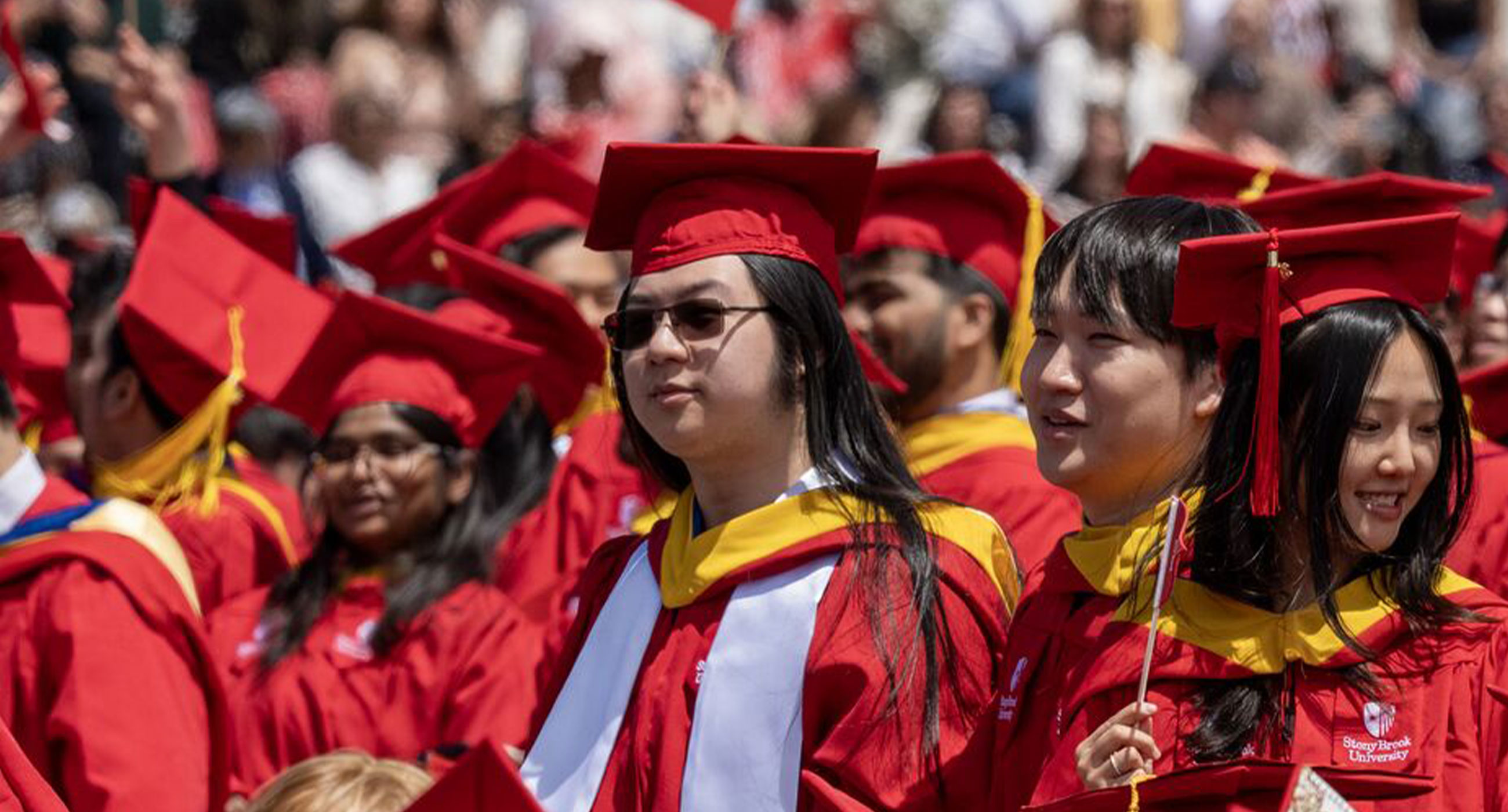 Students in red graduation gowns and caps celebrating at a commencement ceremony.