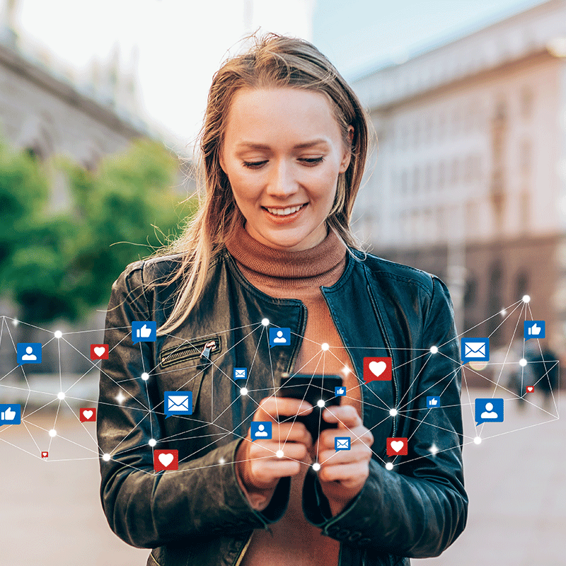 Smiling woman in a leather jacket looks at her phone outdoors.