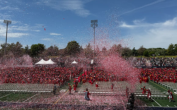 Graduation ceremony with graduates in red gowns under pink confetti.Graduation ceremony with graduates in red gowns under pink confetti.