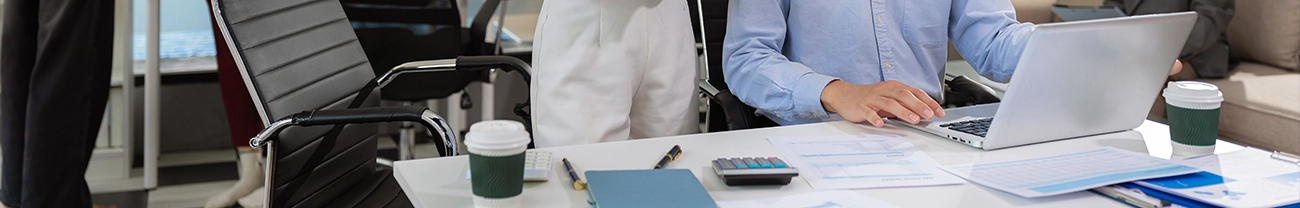 Office setting with a person using a laptop at a desk with documents, a coffee cup, and office supplies.