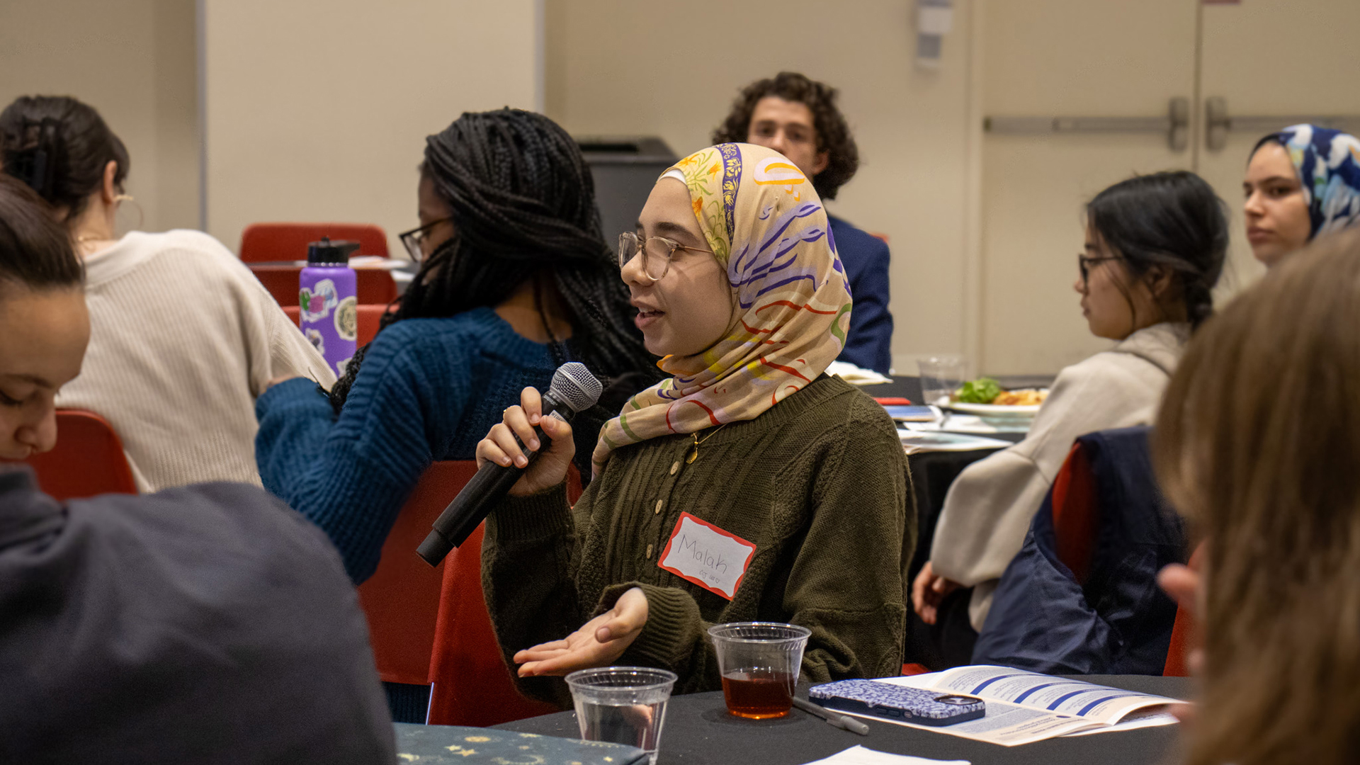 A student speaking into a microphone at a Community Dialogue event.