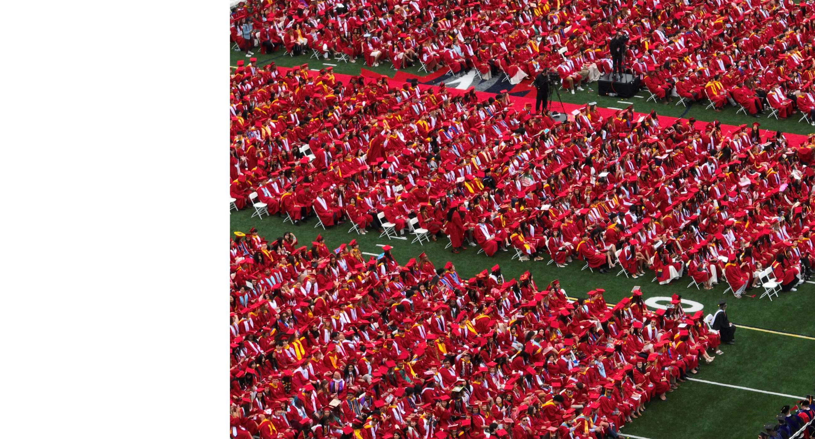 A wide aerial shot of a sea of Stony Brook University graduates in red gowns seated on an outdoor field for commencement.