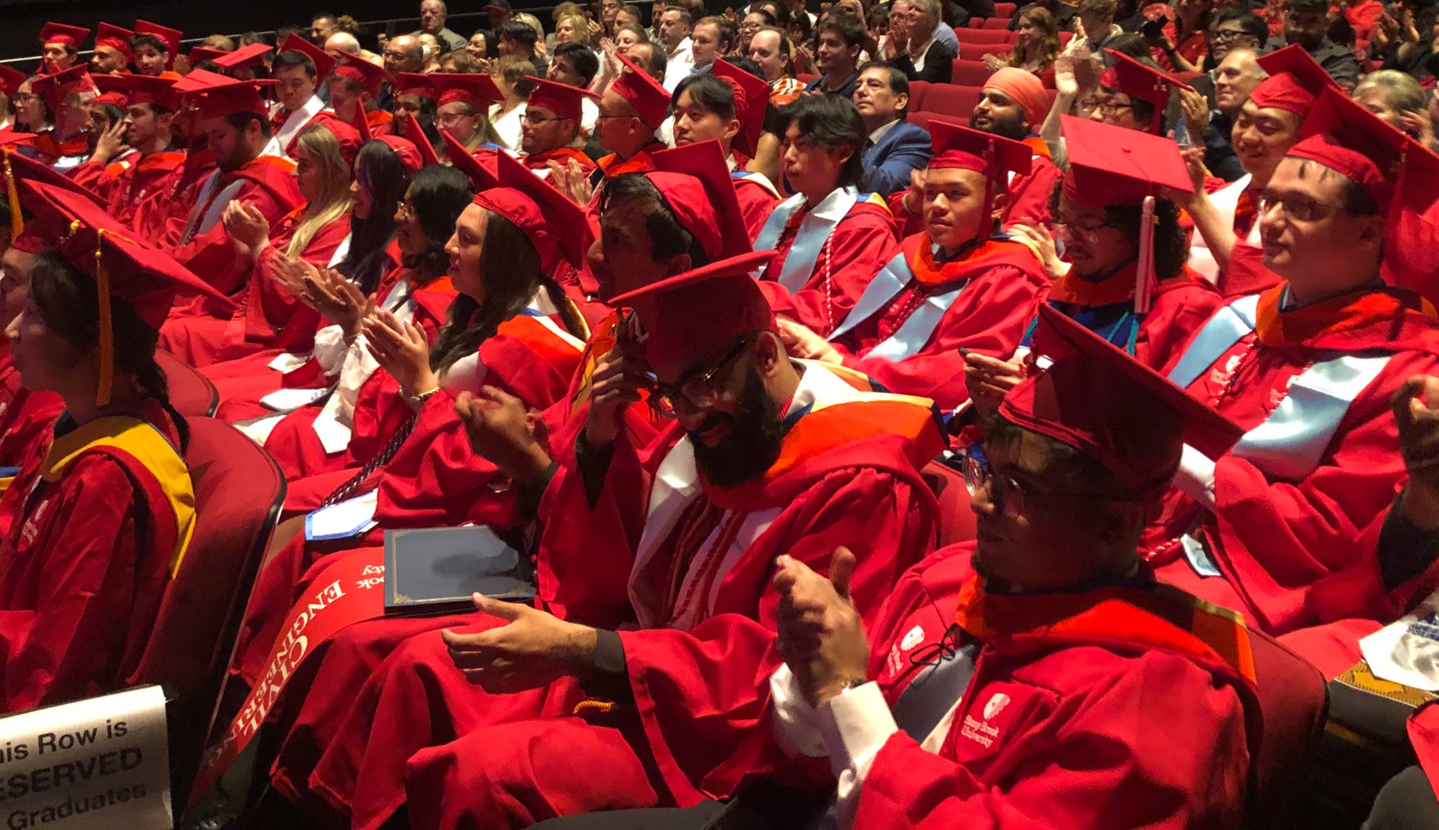 graduate candidates in regalia sitting together in audience apploading
