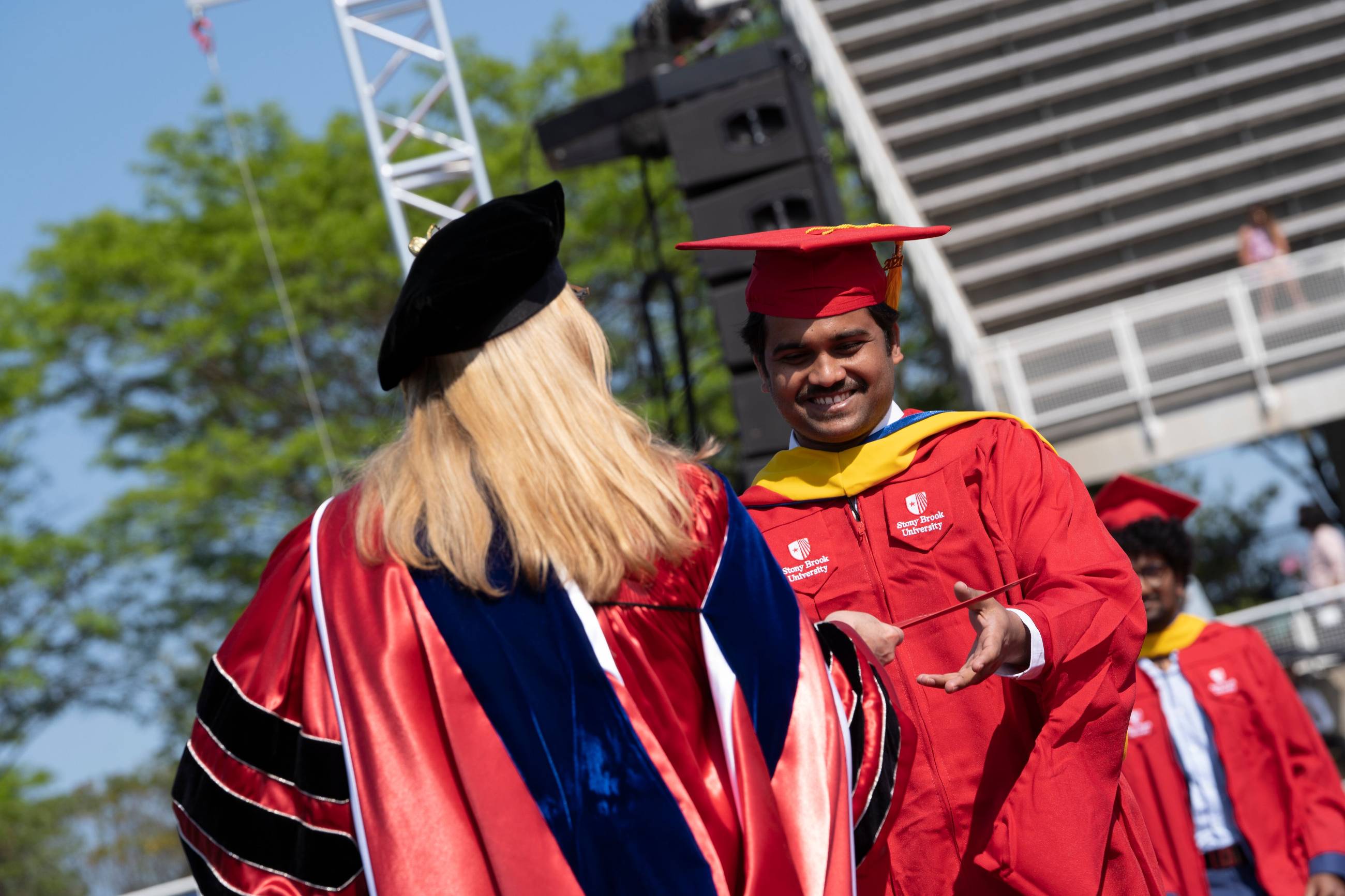 A Stony Brook University graduate receiving their diploma during an outdoor commencement ceremony.