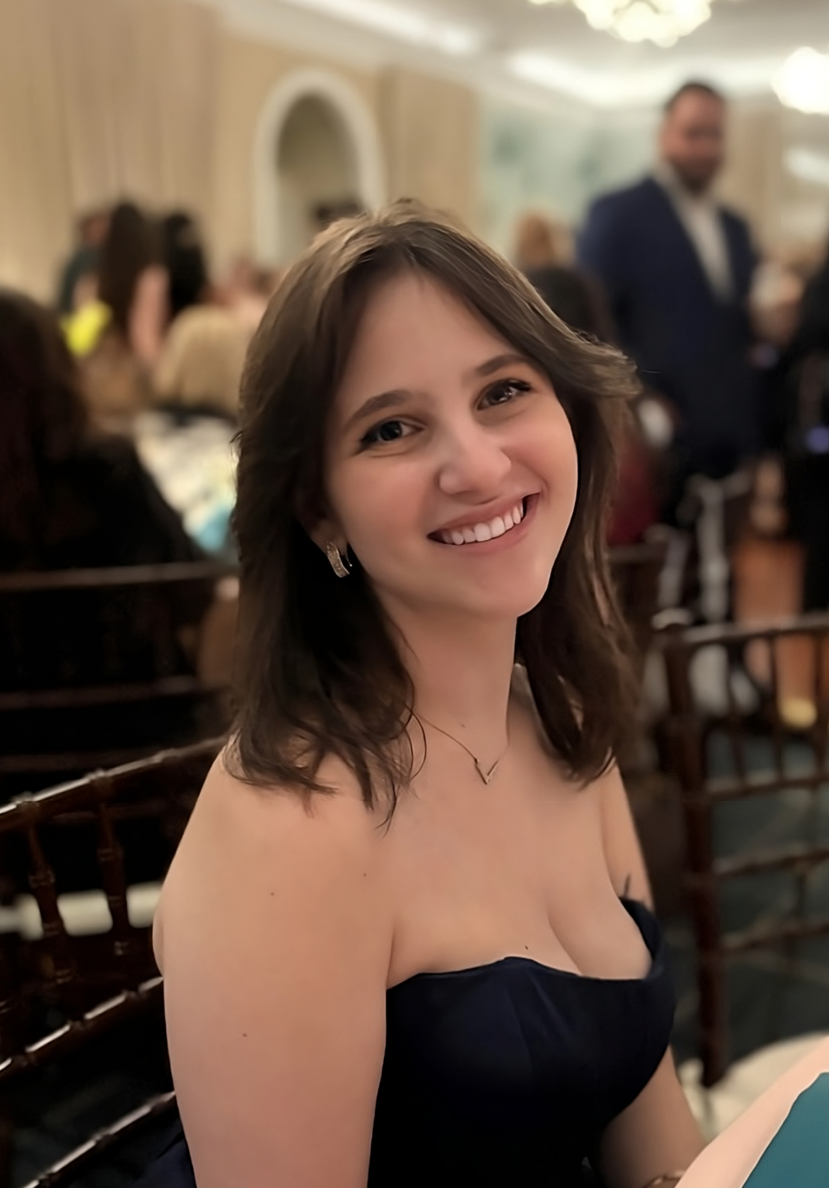 Alexa Zuckerman a smiling person wearing a formal dress sits on a chair in a banquet hall