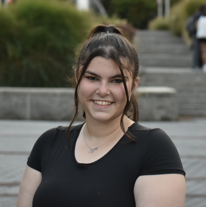 Sophia Goodkin A smiling person stands in front of a fountain outdoors