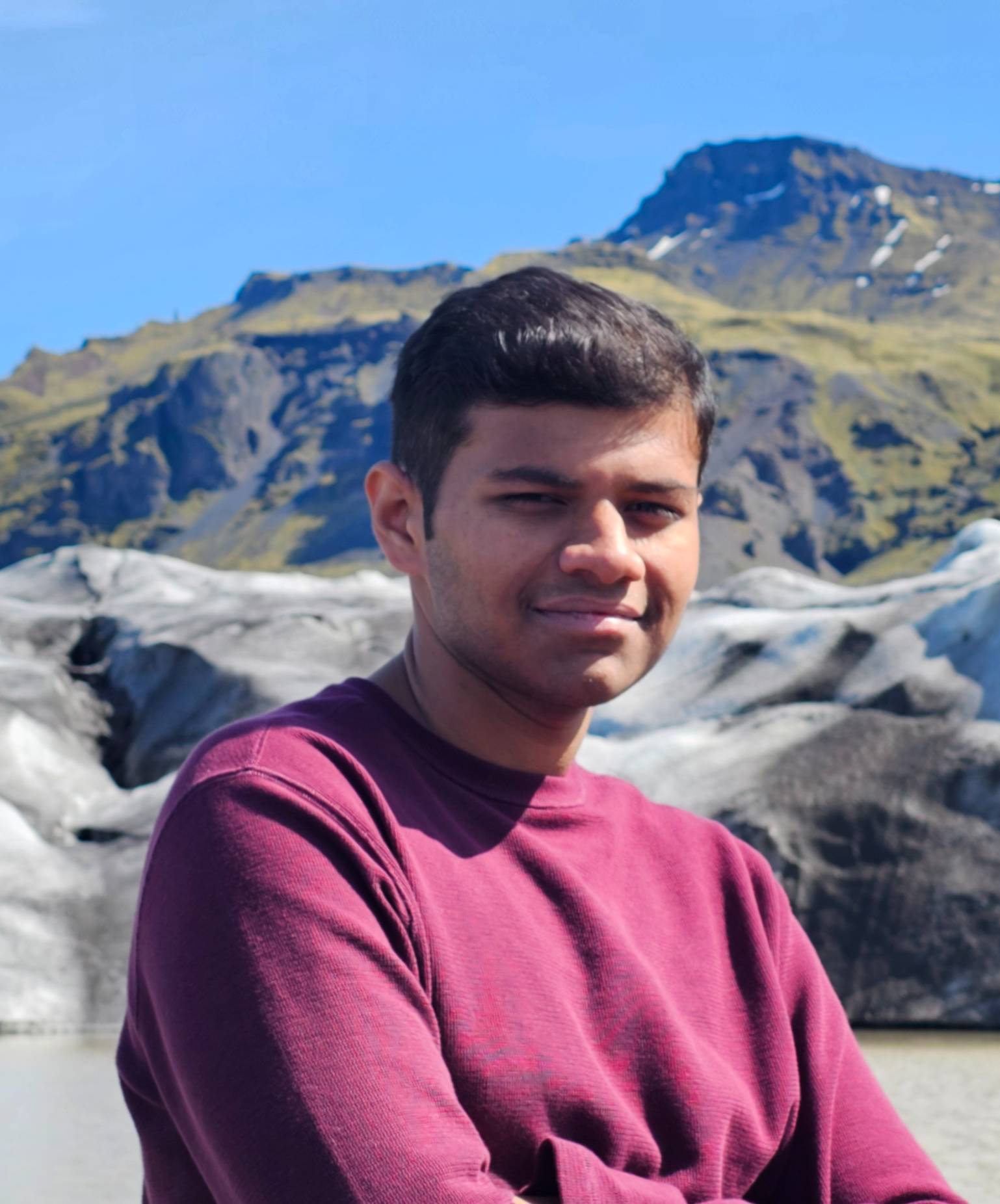 Person in a purple sweater smiling in front of a glacier and lake.
