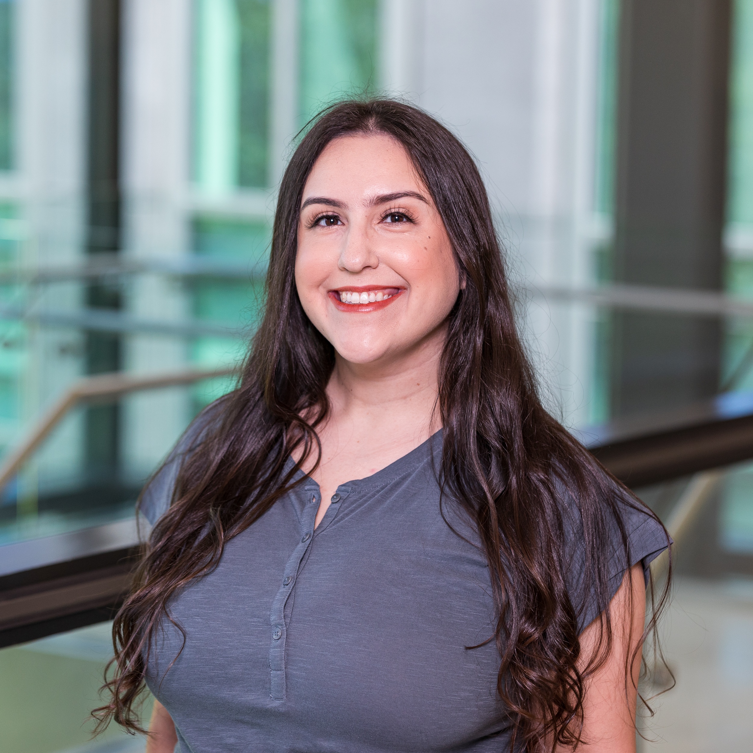 Person smiling in a professional setting with a modern glass background.