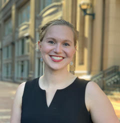 Smiling person in a black dress standing in front of a historical building.