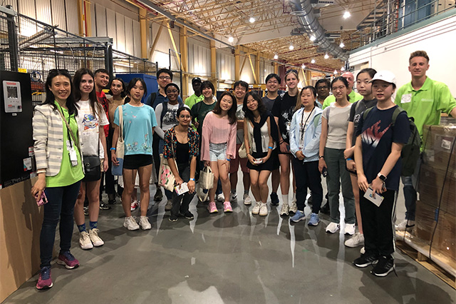 Garcia Program A group of 20 young adults and two guides in green shirts pose inside a warehouse. The atmosphere is cheerful and the setting is industrial.
