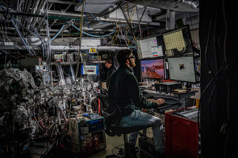 Researchers working at computer monitors amid laboratory equipment and cables.