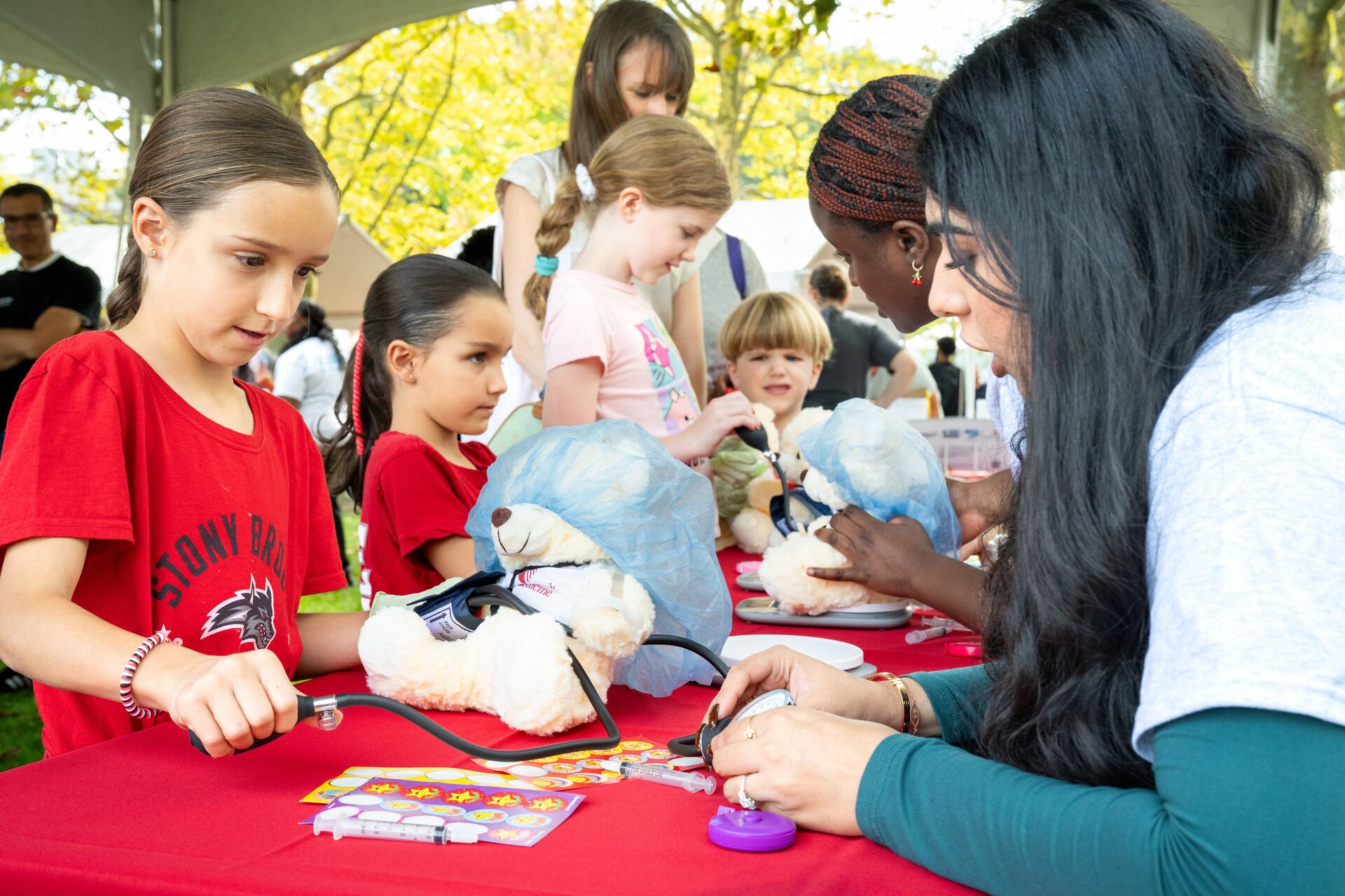 A volunteer helps an attendee demonstrate blood pressure screening on a teddy bear.