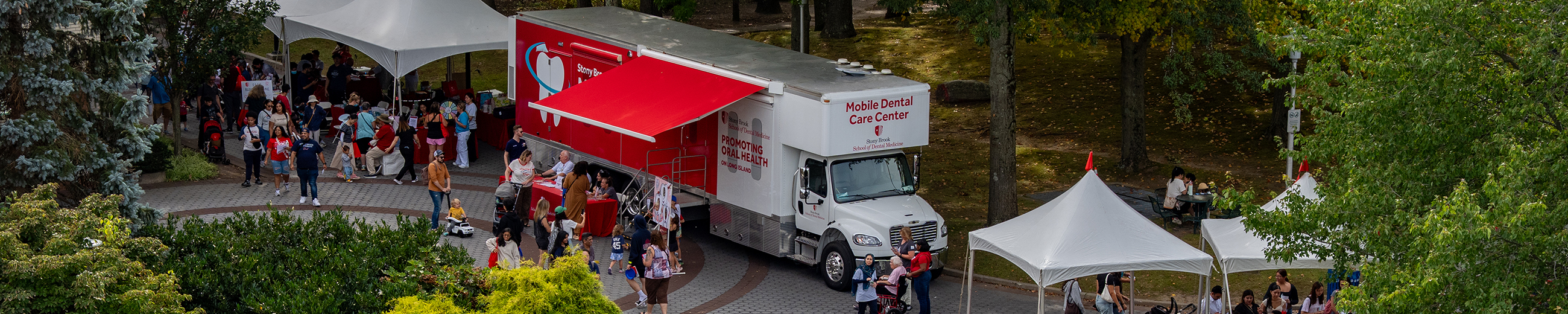 The mobile dental van on display at a festival with groups of people exploring resources at nearby tents.