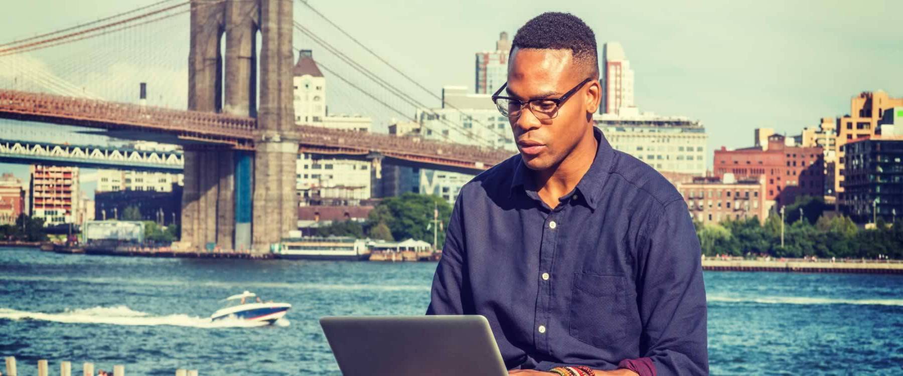 Man working on laptop with the New York skyline behind him