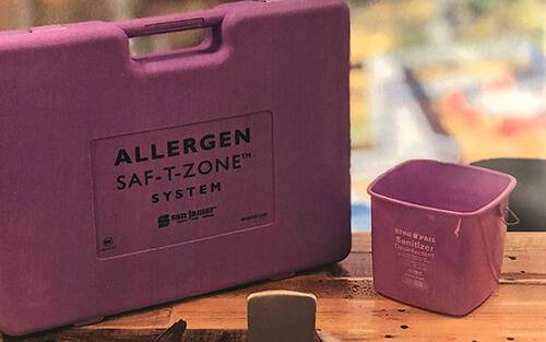 purple kit that reads Allergen Saf-T-Zone and a small bucket on a wooden table