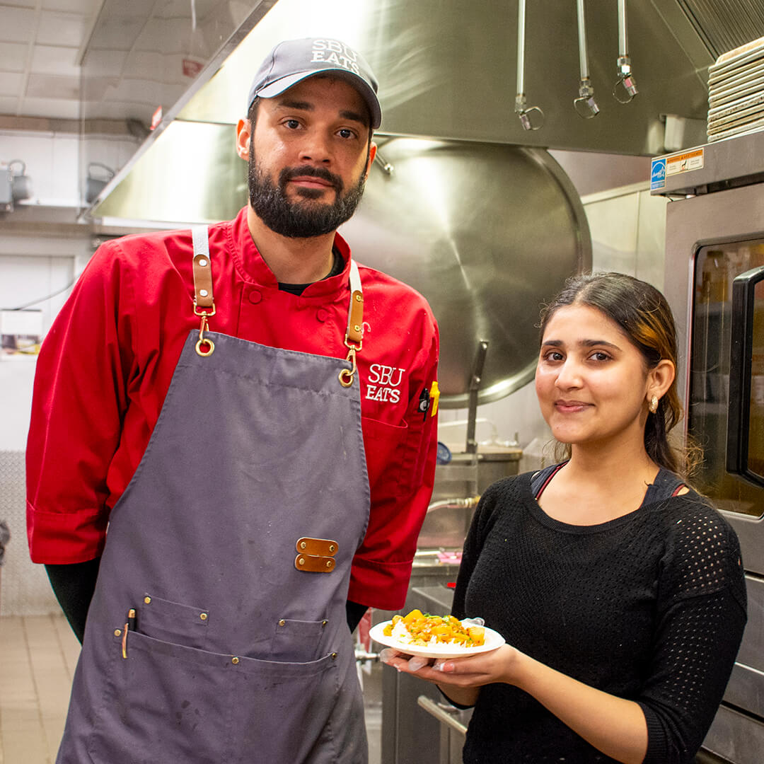 A chef and a woman holding a small plate of curry and rice.