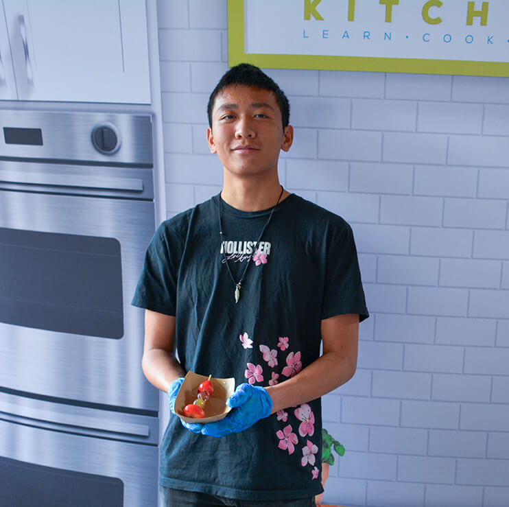Young man in a Hollister t-shirt and blue gloves holding a small tray of fruit