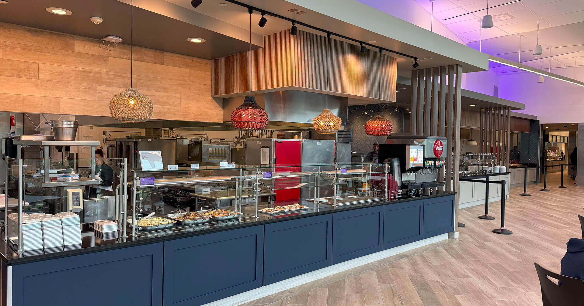 Modern cafeteria with a long serving counter, pendant lights, and visible kitchen area