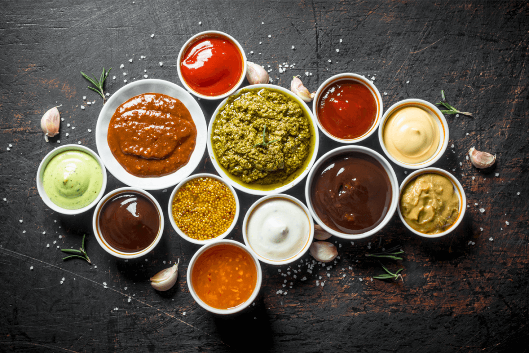 Various small bowls containing different colored sauces on a dark textured surface