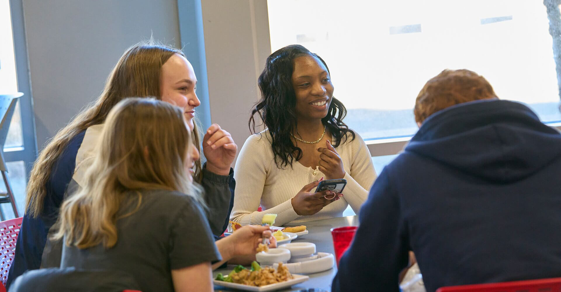 Group of four people sitting at a table, talking and smiling with plates of food in front of them