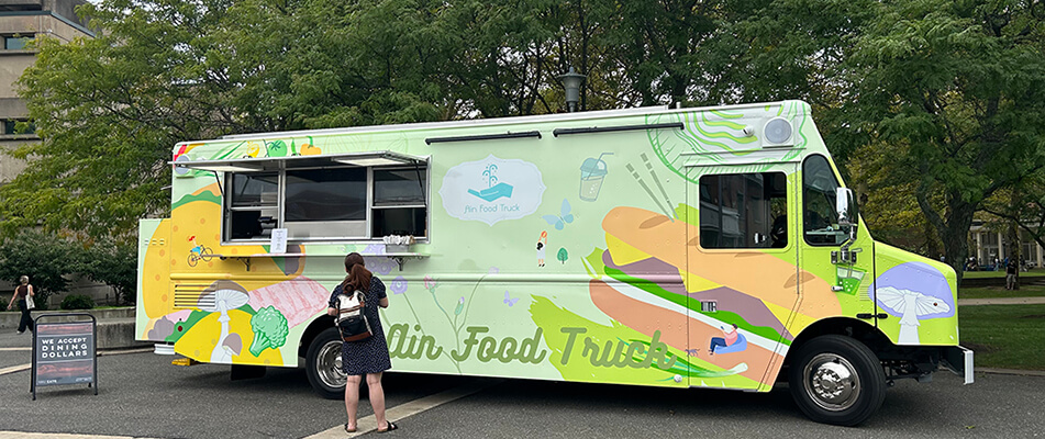 Food truck with colorful illustrations parked in a casual outdoor setting, where a person is interacting at the truck's serving window.