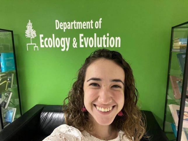 A selfie of Maria in front of a green wall with Department of Ecology & Evolution painted in white.